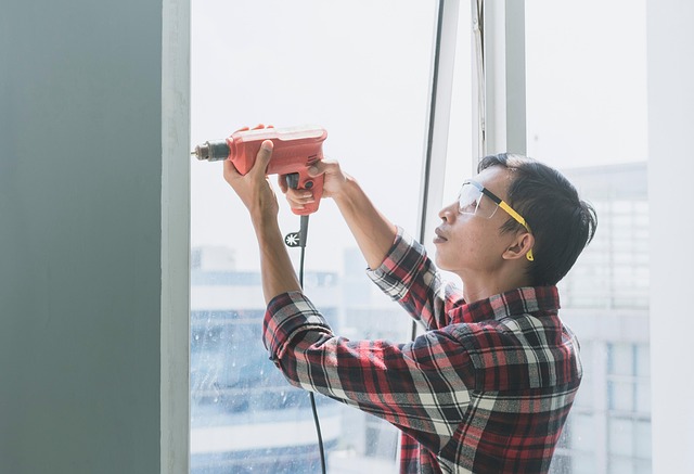 Maintenance person in safety glasses drilling into a window frame during home maintenance