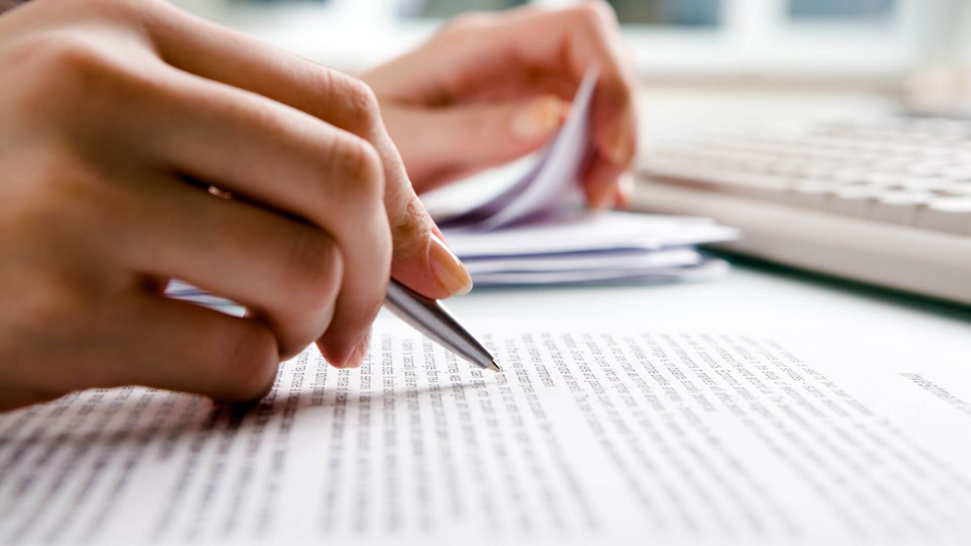 Close-up of a landlord’s manicured hands holding a pen while going through paperwork at a desk.