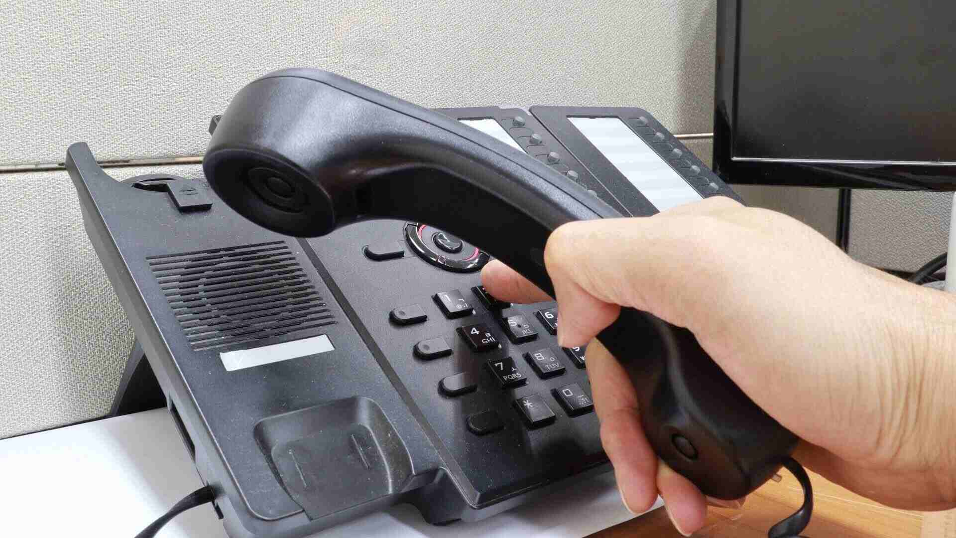 A landlord’s hand dials numbers into their desk landline while holding the attached phone.