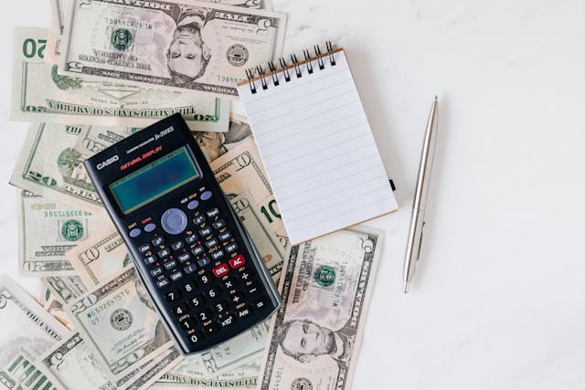 cash, calculator, notepad, and pen laid out on a white table