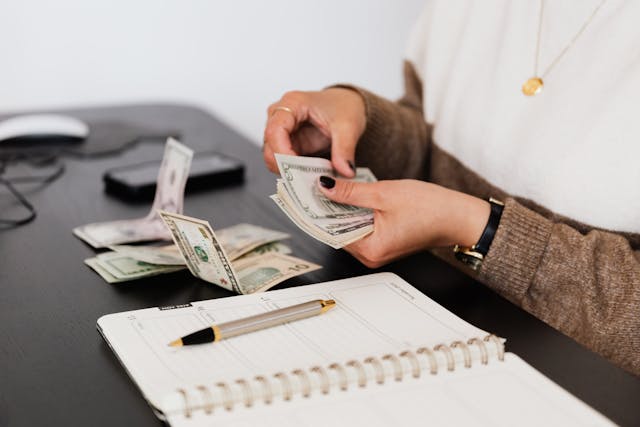 someone counting cash at a desk with an open notebook in front of them
