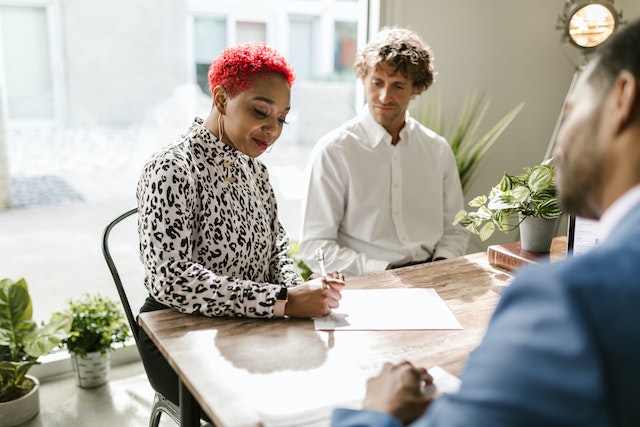 two-tenants-sitting-at-landlords-desk-signing-rental-agreement